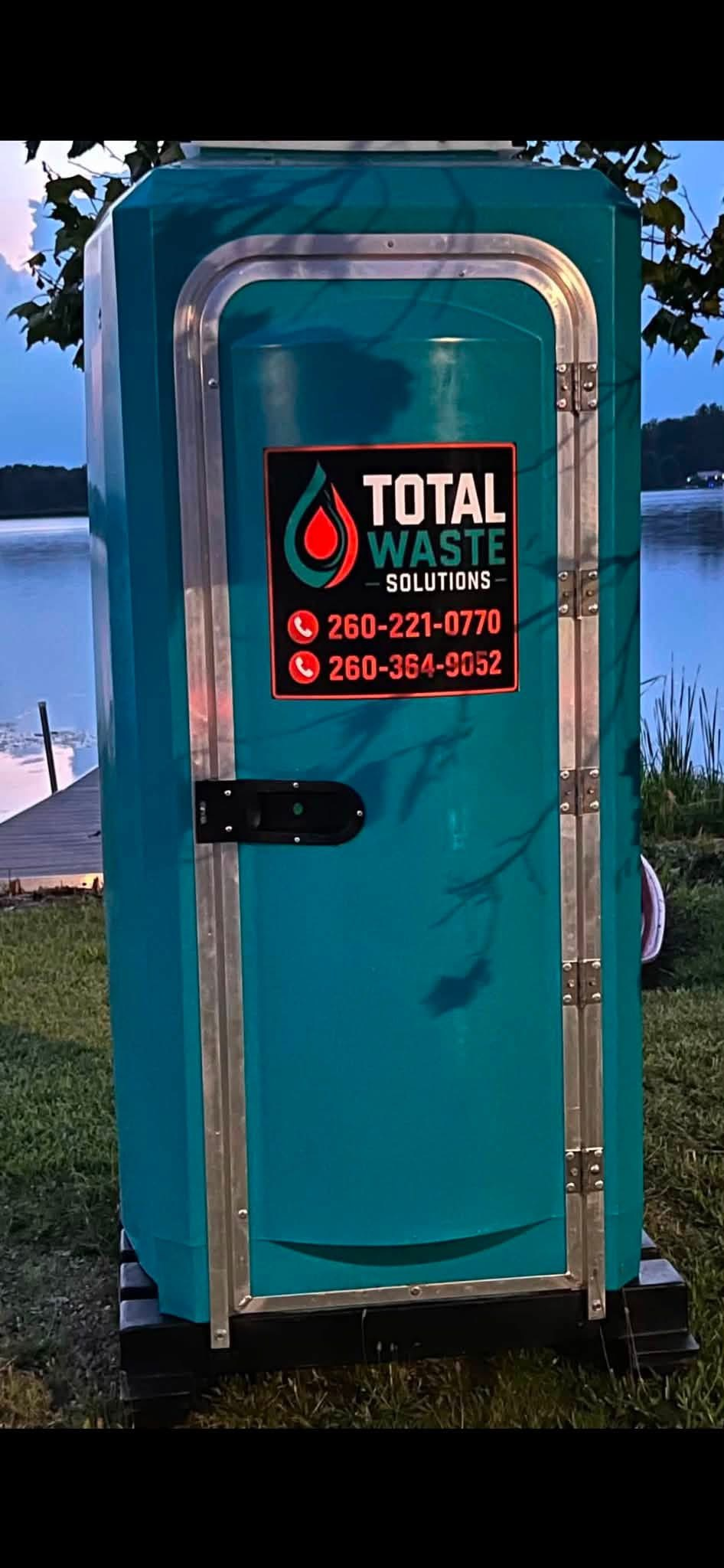 Branded teal Total Waste Solutions portable restroom by a lake